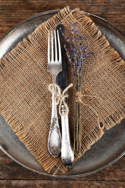 Cubiertos de plata atados con una cuerda en una bandeja de metal con tela de arpillera y flores secas en el fondo de tablones de madera