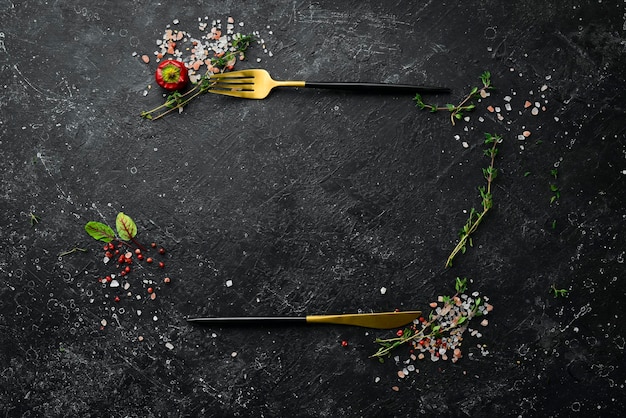 Cubiertos sobre una mesa de piedra negra con verduras y especias. Fondo de alimentos. Vista superior. Estilo rústico.