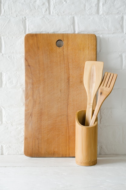 Cubiertos y tabla de cortar de madera o bambú en interior de cocina blanca.