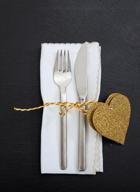 Cubiertos de tenedor y cuchillo para la cena del día de San Valentín atados en la vista superior de fondo negro