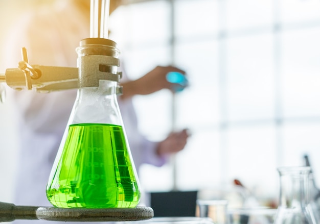 Foto cubilete de medición de cristal del color verde con el fondo del científico en un laboratorio.