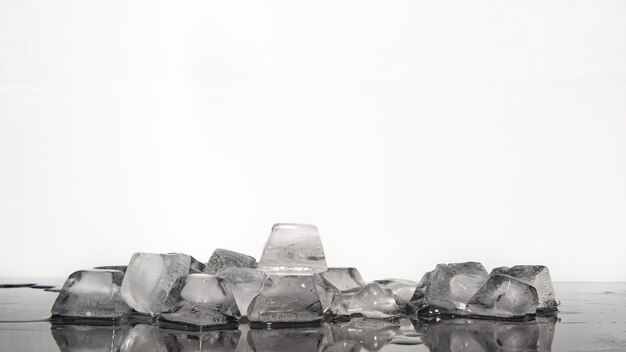 Foto los cubitos de hielo se derriten sobre la superficie reflectante oscura, fondo blanco, enfoque selectivo.