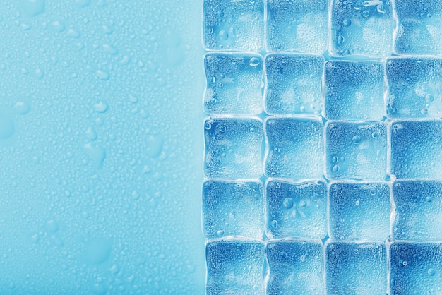 Los cubitos de hielo están esparcidos con gotas de agua esparcidas sobre un fondo azul Cerrar Hielo refrescante