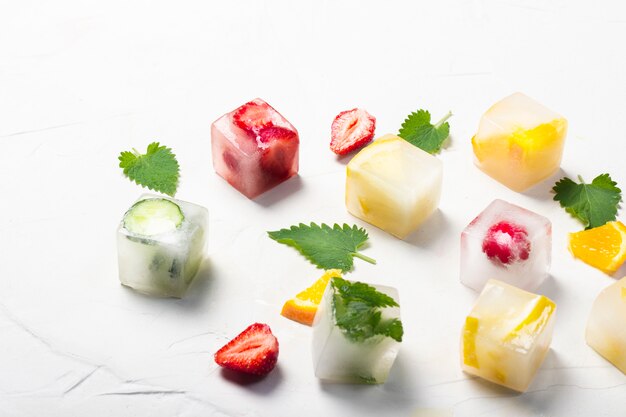 Cubitos de hielo con frutas y hojas de menta sobre un fondo de piedra blanca. Concepto de hielo de frutas, calmar la sed, verano