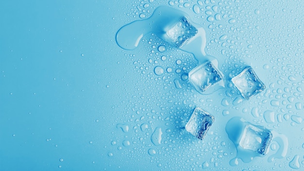 Cubitos de hielo con gotas de agua derretida sobre un fondo azul, vista superior.