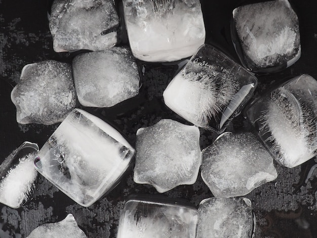 Cubitos de hielo sobre fondo negro mesa con gotas de agua.