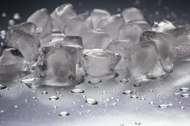 Cubitos de hielo sobre una mesa reflectante con gotas de agua