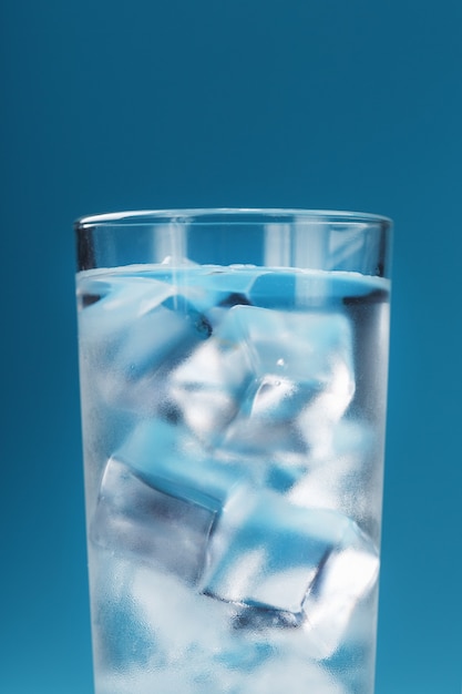 Cubitos de hielo en un vaso con agua cristalina sobre una superficie azul