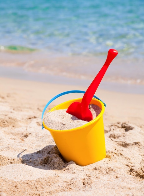 Un cubo de arena amarillo y una pala en una playa