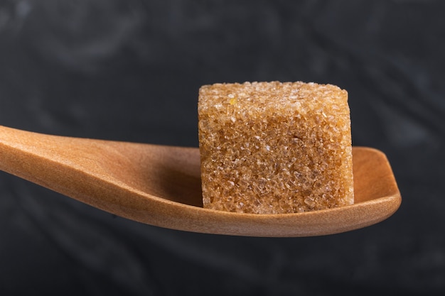 Cubo de azúcar moreno de caña en una cuchara de madera de macro