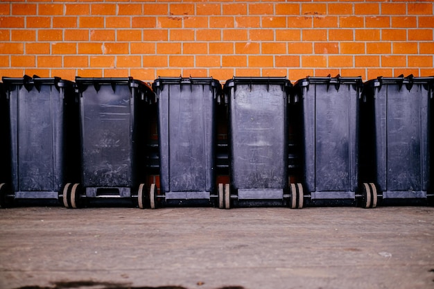 Un cubo de basura en fila frente a una pared de ladrillo