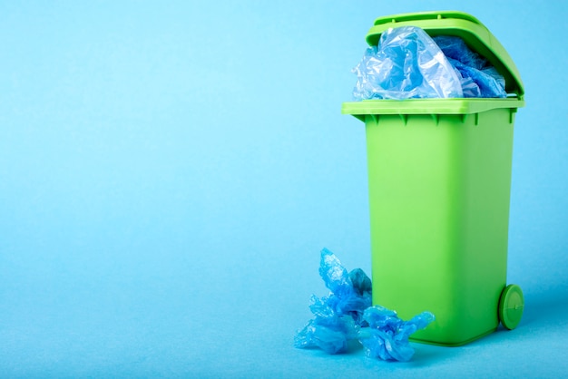 Cubo de basura verde sobre un fondo azul. Polietileno. Reciclaje.