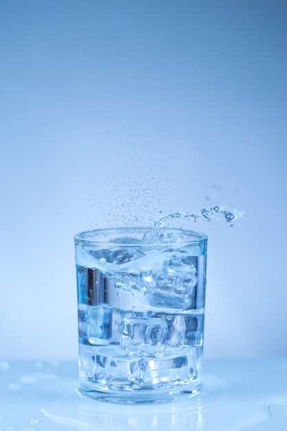 Cubo de hielo cayendo en un vaso de agua