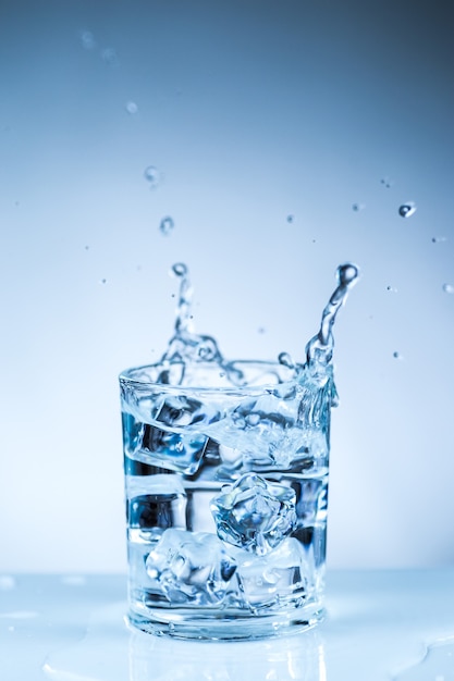 Cubo de hielo cayendo en un vaso de agua