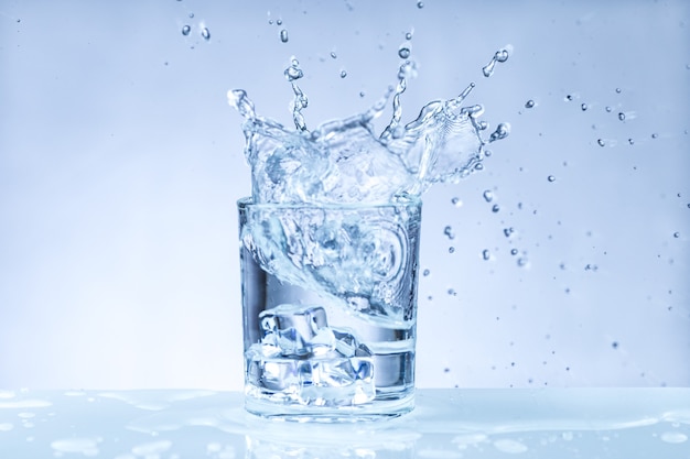 Cubo de hielo cayendo en un vaso de agua