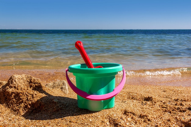 Cubo de juguete para niños de plástico con una cuchara en la orilla arenosa de la playa del mar en un día soleado de verano