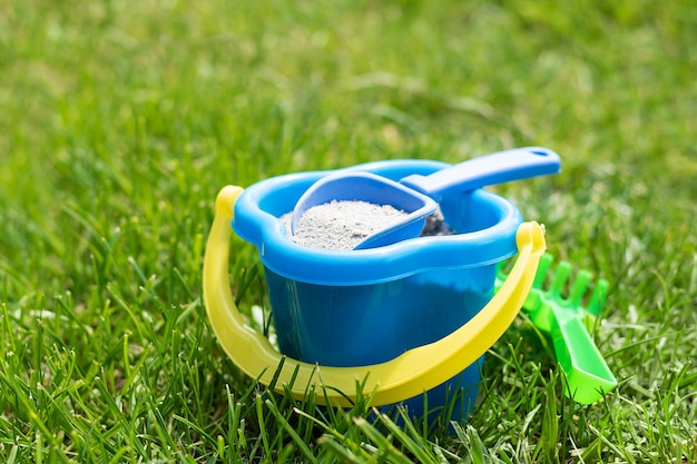 Cubo de juguete de plástico infantil azul con un rastrillo verde en una hierba verde.