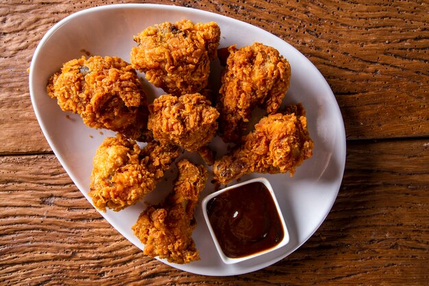 Foto cubo lleno de pollo frito kentucky crujiente con humo y salsa barbacoa sobre fondo marrón. enfoque selectivo.