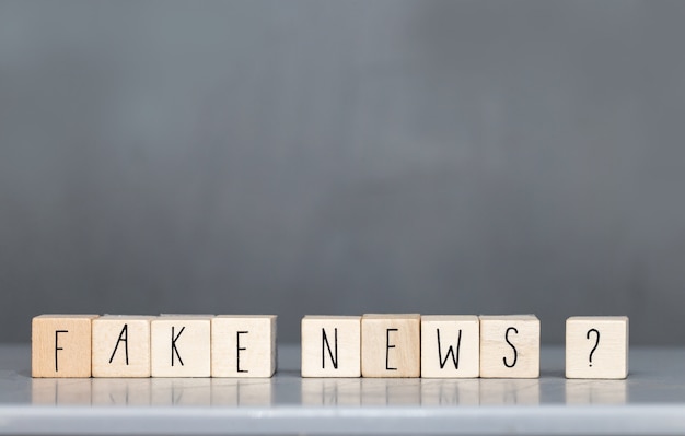 Cubo de madera con las palabras Fake News en la pared gris, redes sociales del concepto Fake News