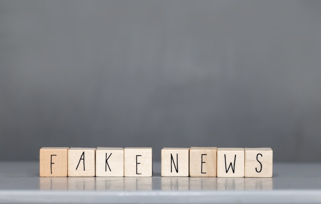 Cubo de madera con las palabras Fake News en la pared gris, redes sociales del concepto Fake News