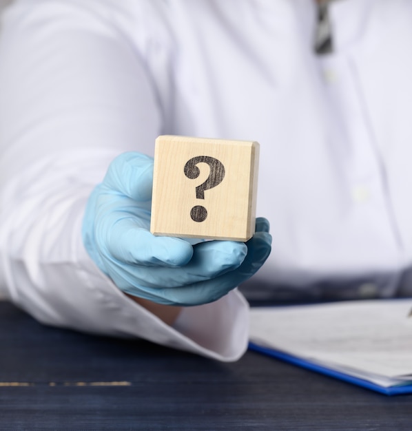 Foto cubo de madera con un signo de interrogación en la mano del médico sobre una superficie azul