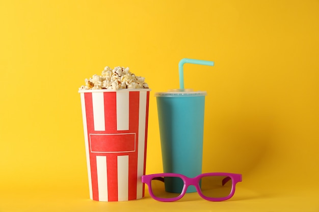 Foto cubo con palomitas de maíz, bebidas y vasos sobre fondo amarillo