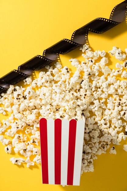 Foto cubo rayado clásico con deliciosas palomitas de maíz y película sobre fondo amarillo