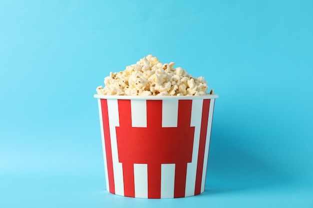 Cubo de rayas con palomitas de maíz sobre fondo azul.