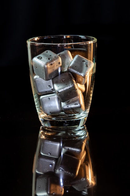 Cubos de acero inoxidable que simulan hielo en vaso de whisky sobre una mesa negra