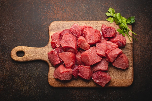 Cubos de carne cruda de ternera para estofado en tabla de cortar de madera