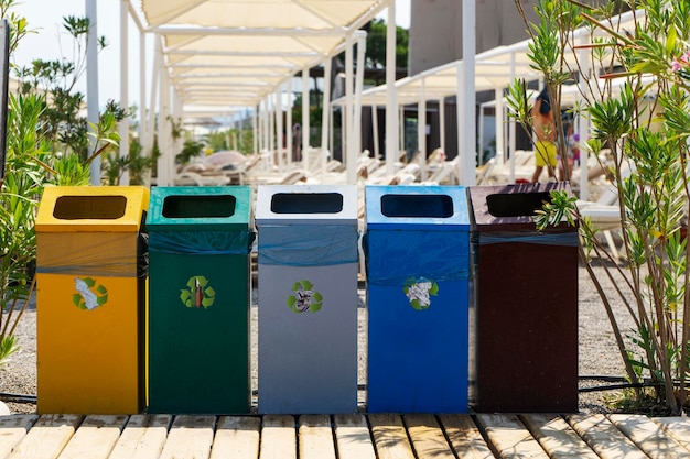 Cubos coloridos para clasificar basura, vidrio, plástico y papel parados en la calle