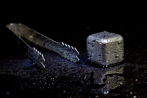 Cubos de aço inoxidável simulando gelo para bebidas refrescantes em uma superfície preta com um reflexo.