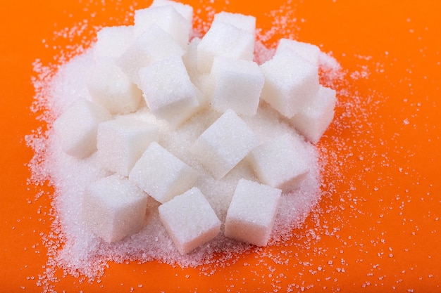 Cubos de açúcar branco e açúcar em um fundo laranja