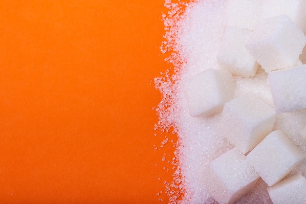 Cubos de açúcar branco e açúcar granulado em um espaço de cópia de fundo laranja