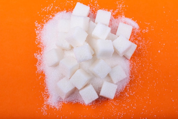 Cubos de açúcar branco e açúcar granulado em um fundo laranja
