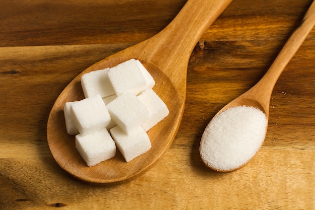 Cubos de açúcar em uma colher de pau e açúcar branco em uma colher de pau