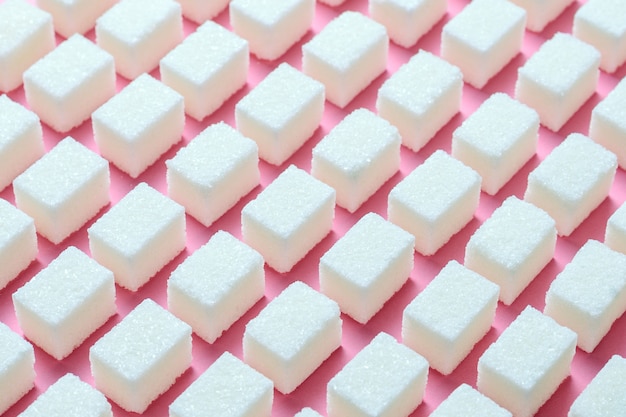 Cubos de açúcar refinado branco a forma geométrica correta em um fundo rosa.