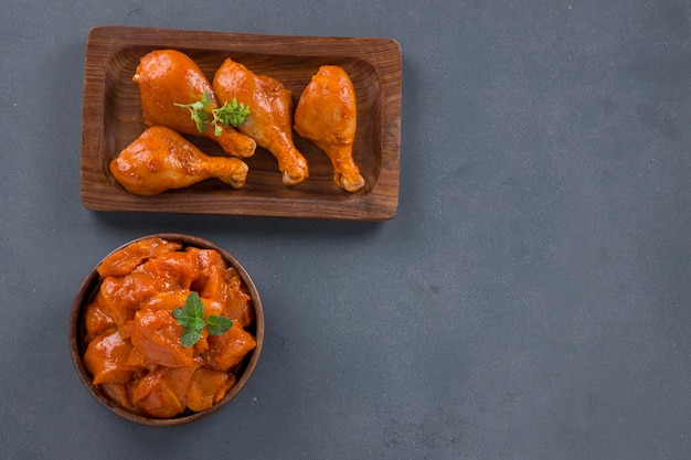 Cubos de frango marinado cru e pernas dispostas em uma louça de madeira guarnecida com coentro fresco e folha de hortelã que é colocada no plano de fundo texturizado cinza.