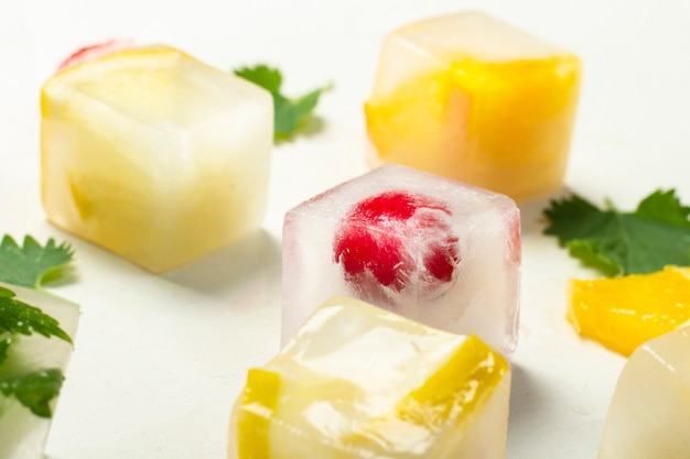 Cubos de gelo com folhas de frutas e hortelã em uma superfície de pedra branca. conceito de gelo de frutas, saciar a sede, verão