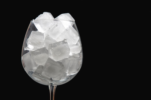 cubos de gelo congelados em um copo de vinho vazio em um fundo escuro