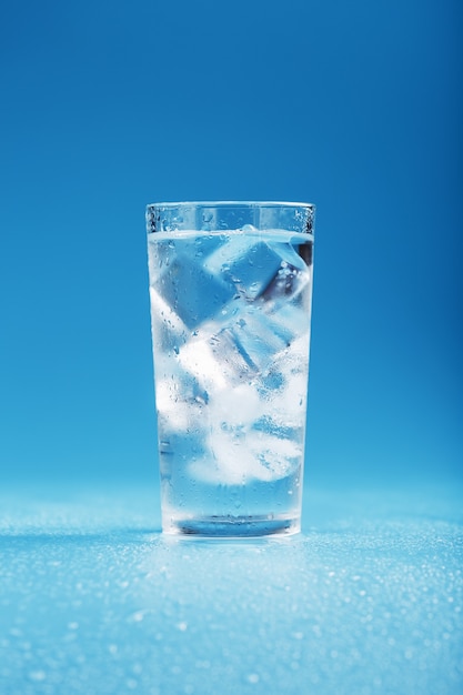 Cubos de gelo em um copo com água cristalina sobre uma superfície azul