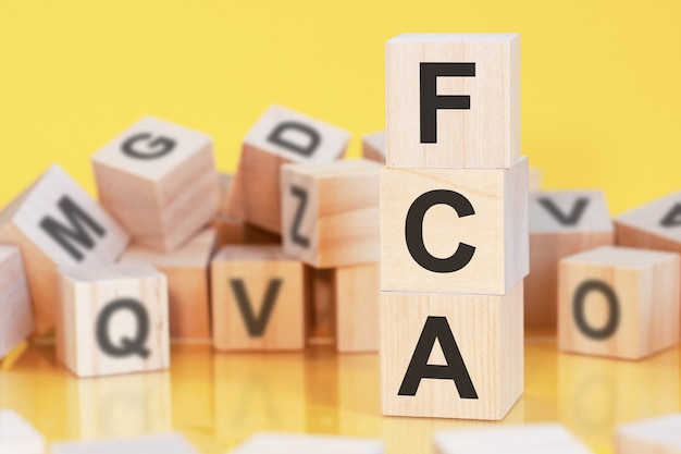 Cubos de madeira com as letras fca dispostos em uma pirâmide vertical, fundo amarelo, reflexo da superfície da mesa, conceito de negócio, fca - abreviação de free carrier