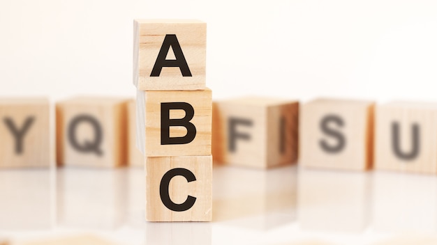 Cubos de madeira com letras ABC dispostas em uma pirâmide vertical, fundo branco, reflexo da superfície da mesa, conceito de negócio. ABC - abreviação de ALWAYS BE CLOSING.