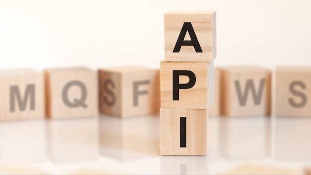 Cubos de madeira com letras api dispostas em uma pirâmide vertical, fundo branco, reflexo da superfície da mesa, conceito de negócio