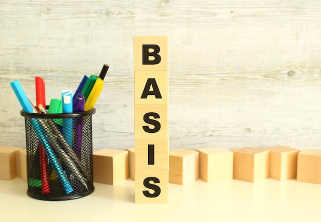 Cubos de madeira empilhados verticalmente com letras na palavra BASIS em uma mesa de trabalho branca em um fundo cinza texturizado