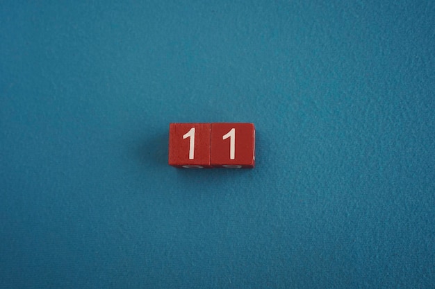 Cubos de madeira Viva Magenta com o número 11 em fundo azul close-up vista de cima Conceito de data ou hora Números brancos 11 em cubos vermelhos fundo de veludo Espaço de cópia para texto ou evento Cubos educacionais