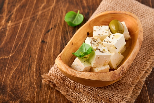 Cubos de queijo feta com alecrim, azeitonas e azeite na superfície de madeira.