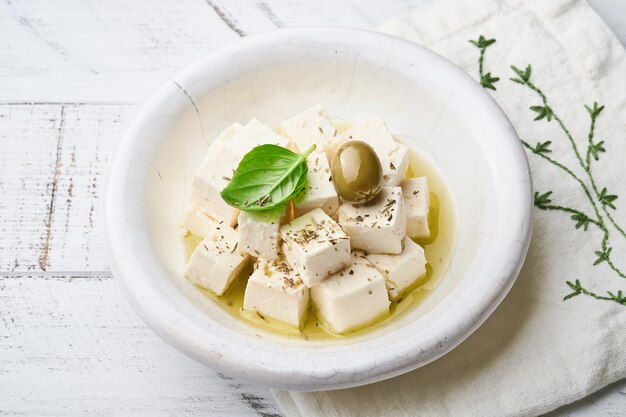 Cubos de queijo feta com alecrim, azeitonas e molho de azeite em tigela branca