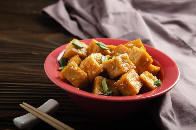 Cubos de tofu fritos crocantes com cebolinha em prato de barro na mesa de cozinha de madeira com guardanapo de lado