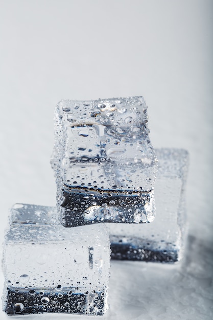 Cubos de hielo en forma de una pirámide con gotas de agua cerca - macro en un fondo blanco.